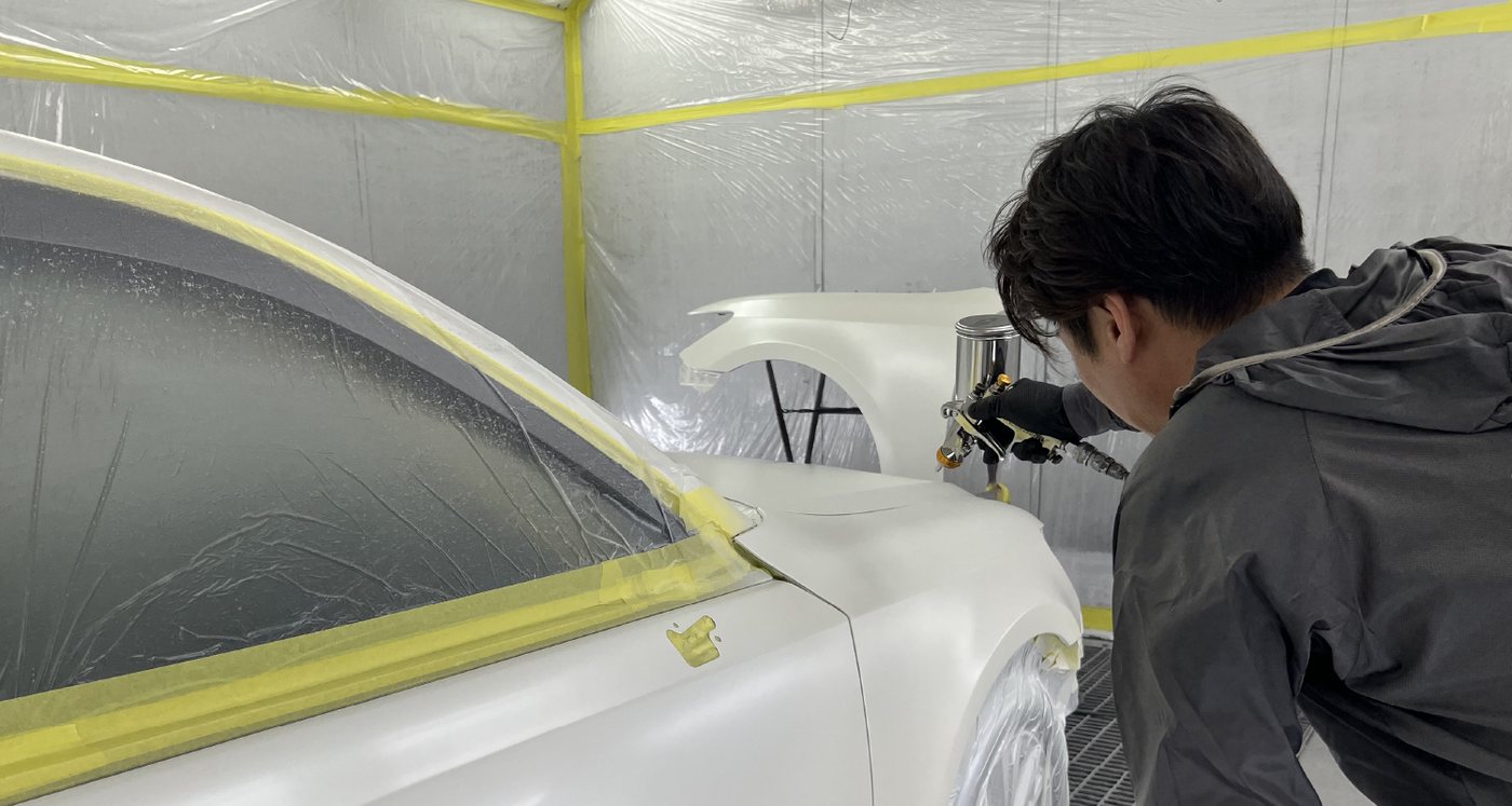 塗装準備をした白い車両へ塗装を施工するスタッフ